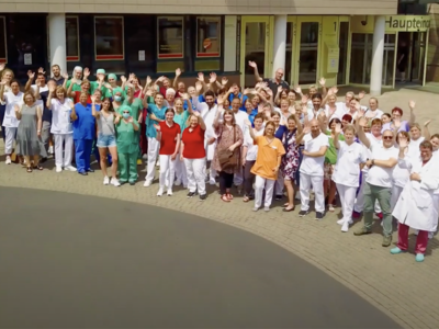 Menschengruppe aus Mitarbeitern, Patienten usw. winken glücklich der Kamera zu, Vogelperspektive