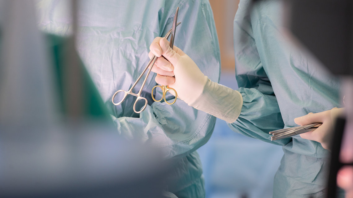 Arzt hät im OP ein Kleingerät, umgeben von mehreren Artzthelfern